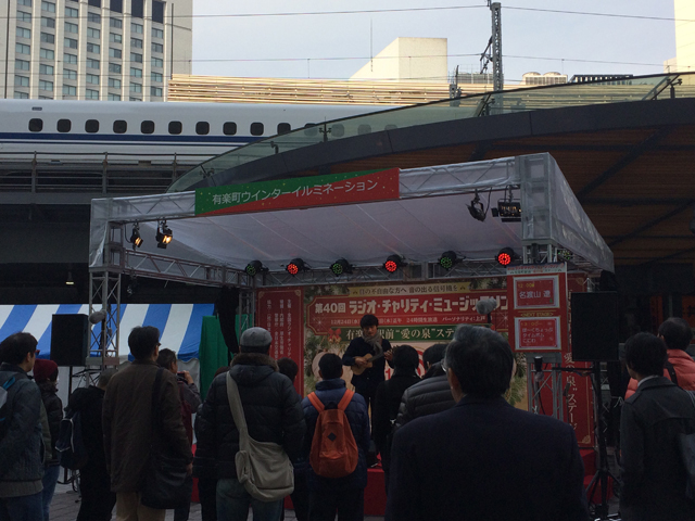 タイトル有楽町駅前愛の泉ステージ 名渡山遼さん演奏中！  本文ついにスタートしました！<br />
ミュージックソン！有楽町駅前も早速盛り上がっております！